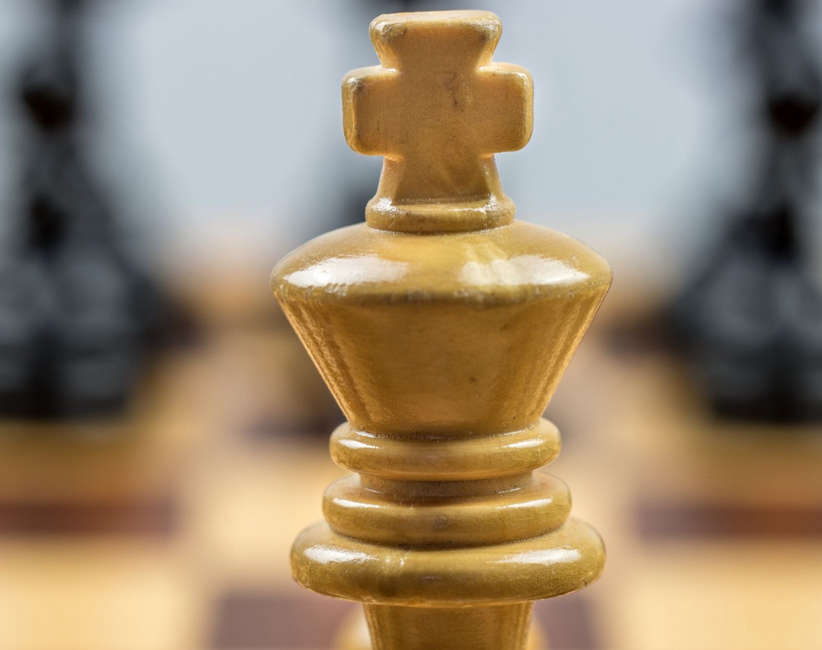 A wooden chess king piece standing alone on a dark board, representing strategic decision making.
