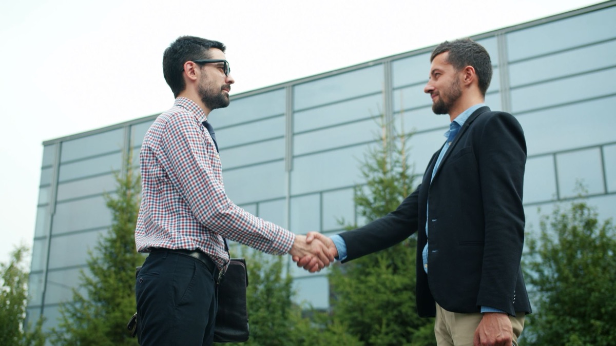 Two hands clasping firmly over a contract document on a polished wooden table.